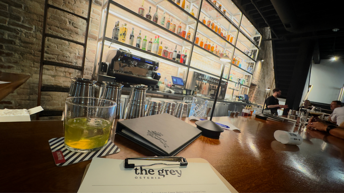 a man holding a martini olive at a cocktail bar with a glass of red wine sitting next to it